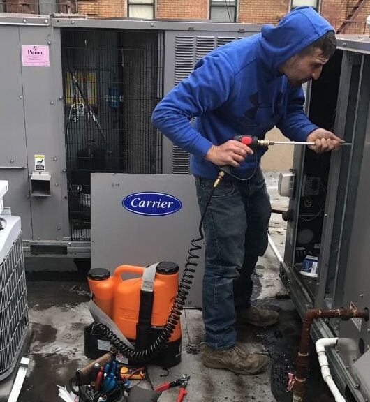 An HVAC technician doing maintenance on a roof-top condensing unit